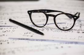 black glasses and black pen sitting on sheet music 